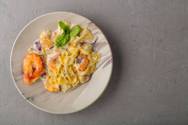 Beton arka planda gri bir tabakta kremalı soslu karidesli makarna. Boşluğu kopyala.
