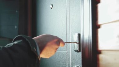 Adamın biri anahtarı anahtar deliğine sokuyor, kilidi açıyor ve adam içeri giriyor.