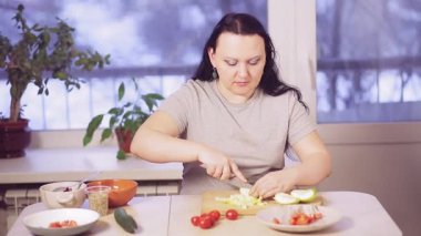 Mutfak masasındaki esmer kadın salata için yeşil elma kesiyor.