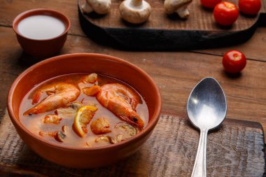 Tom yer elması çorbası, karidesli ve ahşap bir masada bir kaşık dolusu hindistan cevizi sütü mantarı ve domatesin yanında duruyor..