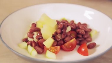 Bir kadının eli kaşıkla ananas parçalarını bir tabak salataya koyar.