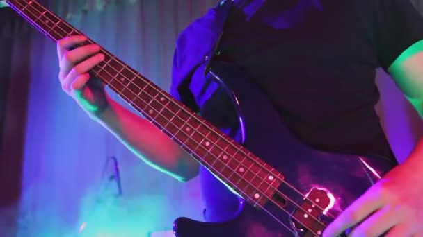 Un uomo tiene una chitarra nella mano destra nella luce al neon suona una chitarra elettrica sul set di un concerto senza volto. — Video Stock