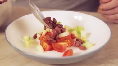 Kaşıklı bir kadın eli kırmızı fasulyeyi bir tabak salataya çevirir.
