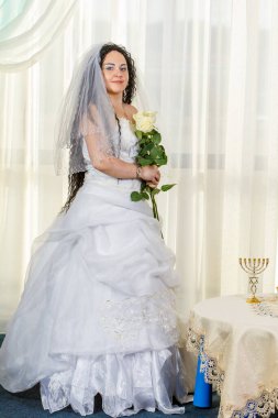 Musevi bir gelin salgın sırasında bir salgın sırasında bir sinagogda çiçeklerle bir masada duruyor, bir buket çiçek ve sağlık maskesi takıyor.