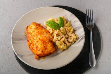 Fırınlanmış tavuk göğsü ve salata tabakta ıspanakla süslenmiş gri arka planda gri bir çatalın yanında yuvarlak siyah bir standın üzerinde..