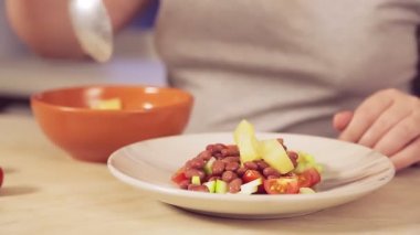 Bir kadının eli kaşıkla ananas parçalarını bir tabak salataya koyar.