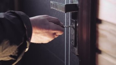 Adamın biri anahtarı anahtar deliğine sokuyor, kilidi açıyor ve adam içeri giriyor.
