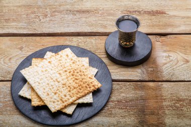 Ahşap bir masa, matza ve siyah yuvarlak altlıklarda bir bardak kiraz şarabı..