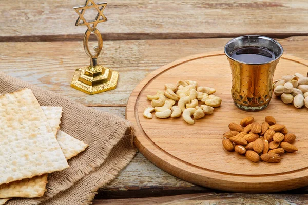 Matzah and a round board with nuts and a glass of kiddush wine on a wooden table and a menorah.