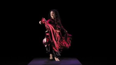 Kırmızı elbiseli, uzun saçlı çıplak ayaklı çingene kadın siyah arka planda dans ediyor.