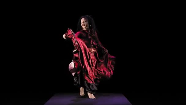 Босоногая цыганка с длинными волосами в красном костюме танцует на черном фоне — стоковое видео