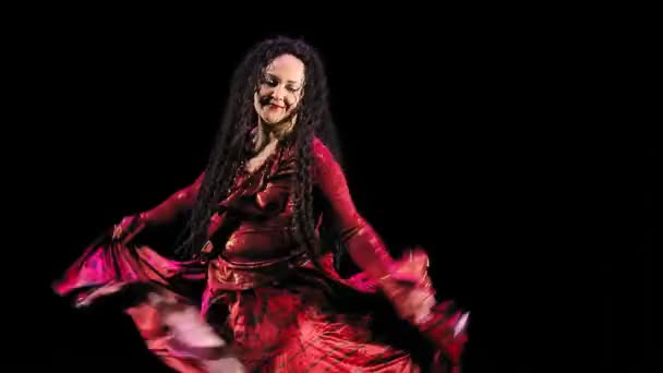 Een mooie zigeunerin met lang haar in een rood pak danst brandend op een zwarte achtergrond — Stockvideo