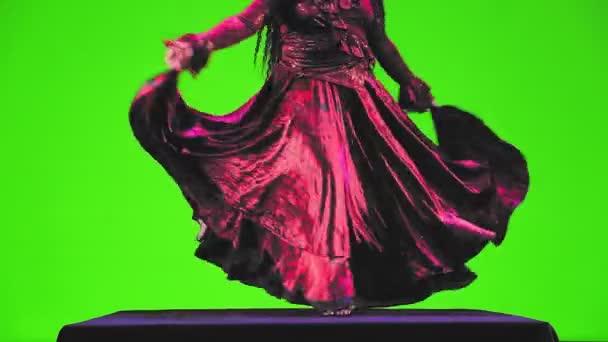Босоногая цыганка без лица с длинными черными волосами в красном костюме танцует на зеленом фоне. — стоковое видео