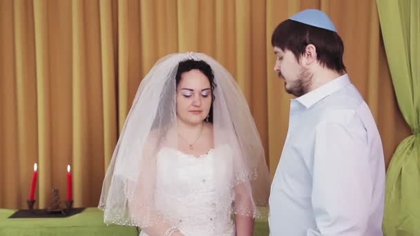 Durante a cerimônia do chuppah, uma noiva e um noivo judeus em uma sinagoga colocam um anel no dedo indicador das noivas.. — Vídeo de Stock