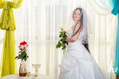 Sinagogda peçeli bir Yahudi gelin salgın sırasında bir chuppa töreninden önce bir buket çiçek ve sağlık maskesi takıyor. Yatay fotoğraf