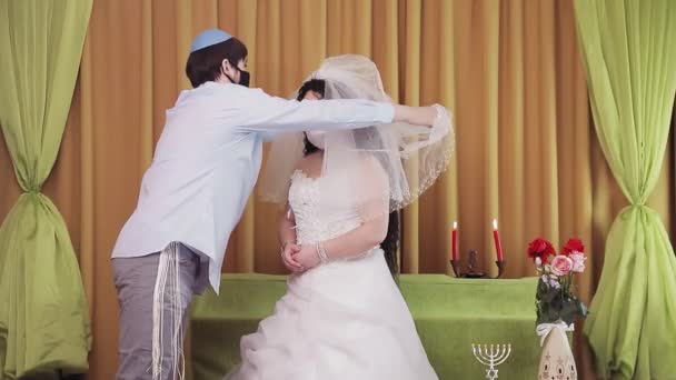 礼拝中 ユダヤ人の花嫁と新郎が会堂で守護マスクを着用し 花嫁の顔からベールを持ち上げます 計画全体 — ストック動画