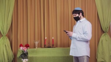Chuppah töreninden önce, bir sinagog salonunda koruyucu maskeli bir Yahudi damat telefonla bir SMS çevirir. Genel plan