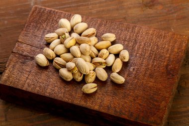 Ahşap bir masanın üzerindeki kare tahtaya saçılmış fıstıklı fındık. Yatay fotoğraf