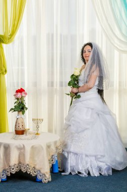 Mutlu bir Yahudi gelin elinde bir buket beyaz gülle Chuppa seremonisi masasının önünde duruyor. Dikey fotoğraf