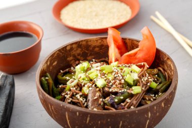 Mantarlı soba ve hindistan cevizi kabuğunda susam tohumlu yeşil fasulye sarımsak ve soya sosunun yanında gri beton arka planda. Yatay fotoğraf