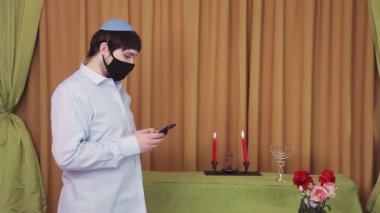 Chuppah töreninden önce, bir sinagog salonunda koruyucu maskeli bir Yahudi damat telefonla bir SMS çevirir. Ortam planı