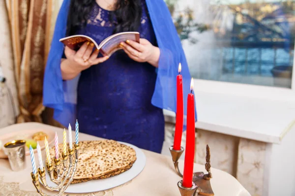 Uma mulher judaica sem rosto na mesa de Páscoa Seder lê a Páscoa Haggadah. — Fotografia de Stock