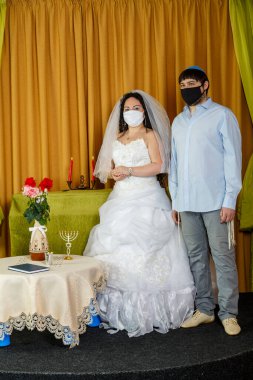 Sinagogdaki chupa töreni sırasında maskeli Yahudi gelin ve damat yan yana dururlar. Dikey fotoğraf