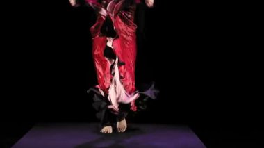 Yüzü uzun, siyah saçlı, kırmızı elbiseli çıplak ayaklı bir çingene kadın siyah arka planda ateşli bir şekilde dans ediyor. Genel plan