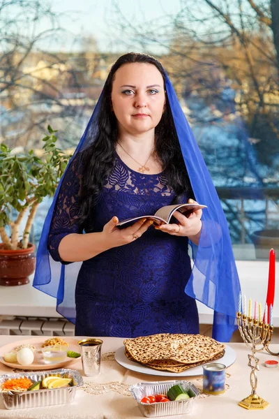 一位头戴蓝色披风的犹太妇女在逾越节的种子桌上读逾越节的 哈加德 垂直照片 — 图库照片