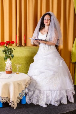 Duvağı olan beyaz bir gelinlik içinde Yahudi bir gelin çiçeklerle dolu bir masada duruyor ve chuppah seremonisinden önce mutlu bir aile hayatı için dua ediyor..