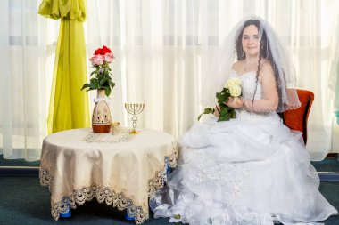 Yüzü beyaz güllerle kaplı neşeli bir Yahudi gelin, çiçeklerle dolu bir masada Huppa töreni yapmadan önce sinagogda oturur..