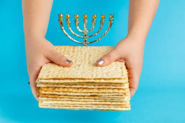 A stack of matzo in female hands on a blue background near the menorah. — Stock Photo, Image