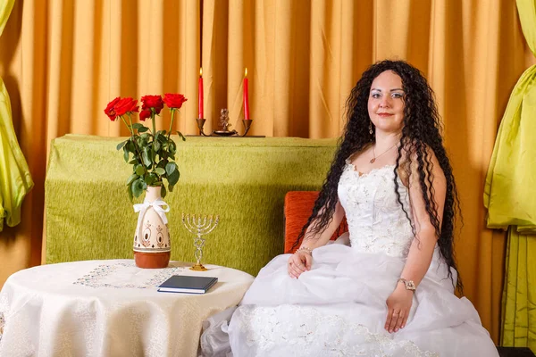 婚礼前，一位身着白色婚纱婚纱的犹太新娘坐在鲜花盛开的桌旁. — 图库照片