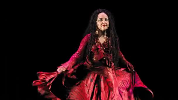 En vacker zigenare kvinna med långt svart hår i en röd kostym dansar glödande på en svart bakgrund. — Stockvideo