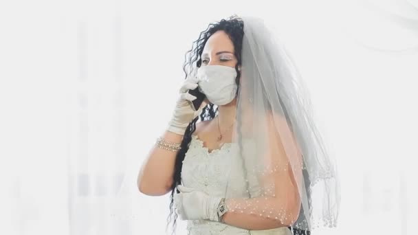 Een Joodse bruid in een trouwjurk en sluier met een medisch masker in een synagoge voor de chupah ceremonie aan de telefoon spreekt — Stockvideo
