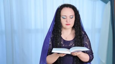 Kafasında pelerin olan Yahudi bir kadın yemekten önce Kabala Şabat 'ı şarap için masada okur.