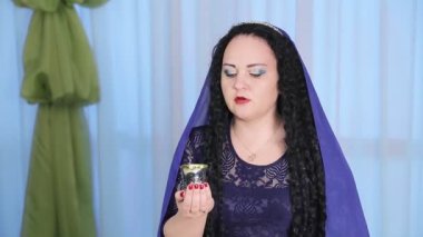 Kafasında pelerin olan Yahudi bir kadın Şabat yemeğinde masada şarap içer.