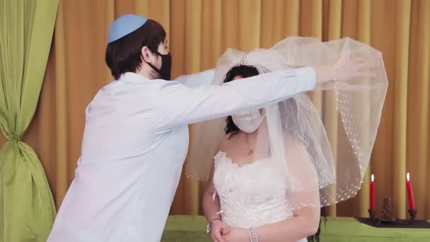 Durante la ceremonia de chuppah, una novia y un novio judíos con máscaras protectoras en una sinagoga levanta el velo de la cara de las novias — Vídeo de stock