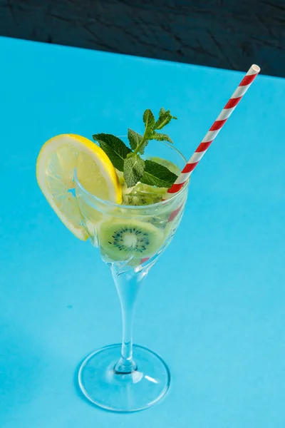 Kiwi koktajl ozdobiony cytryną i miętą w szklance na serwetce na niebieskim tle. — Zdjęcie stockowe