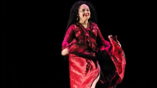 Красива циганка з довгим волоссям у червоному костюмі запально танцює на чорному тлі — стокове відео