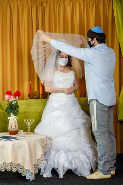 Sinagogdaki chuppah töreni sırasında, maskeli gelin ve damat gelinin yüzündeki örtüyü kaldırır. Dikey fotoğraf