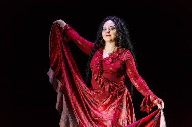 Çingene kadın yalınayak, uzun siyah saçlı, siyah arka planda kırmızı bir elbiseyle dans ediyor. Yatay fotoğraf