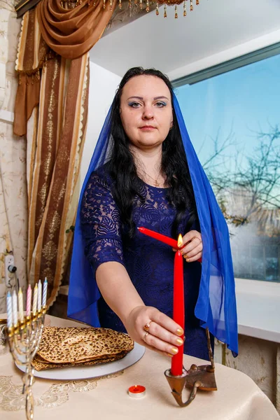 在逾越节的餐桌前 一位头戴蓝色披风的犹太妇女正在点燃一支蜡烛 垂直照片 — 图库照片