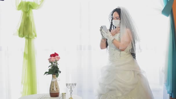 Μια Εβραία νύφη με νυφικό και ένα πέπλο φορώντας ιατρική μάσκα σε αίθουσα συναγωγής απαντά σε μήνυμα πριν την τελετή Τσάππα. — Αρχείο Βίντεο