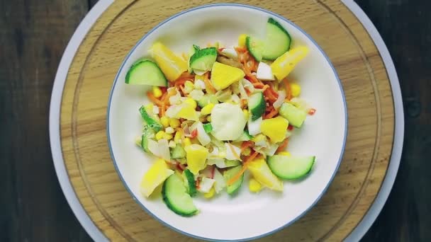 Salade met krab vlees versierd met komkommer en sinaasappel in een bord op een houten statief draait in een cirkel bovenaanzicht. — Stockvideo