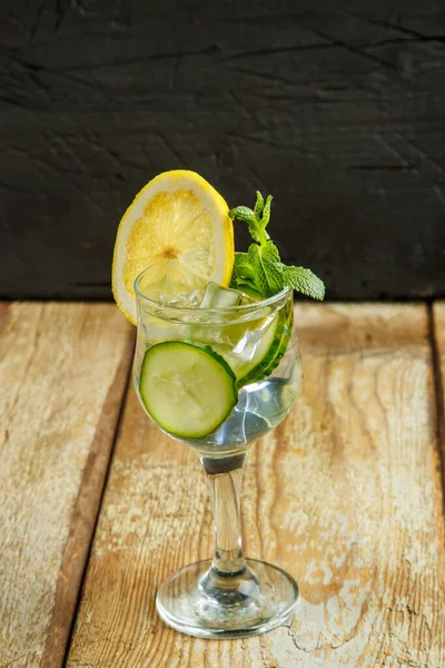 Коктейль з огірком вода з лимоном і м'ятою в склянці на дерев'яному столі на чорному тлі . — стокове фото