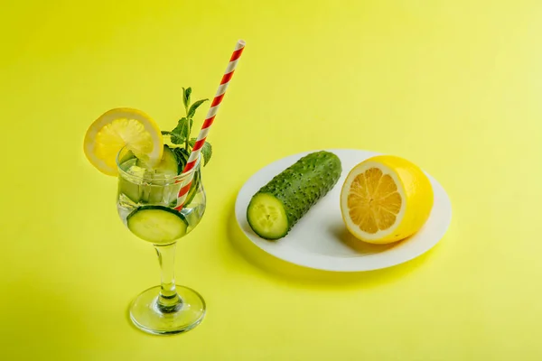 Коктейль з огірком вода з лимоном і м'ятою в склянці на серветці на жовтому тлі поруч з огірками і лимоном на серветці . — стокове фото