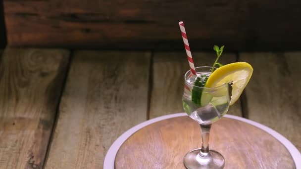 Un cocktail con menta di cetriolo e limone in un bicchiere su un gambo su uno sfondo di legno ruota in cerchio — Video Stock