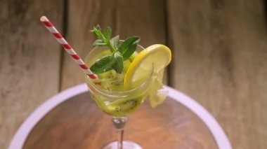 Naneli ve limonlu bir kokteyl, tahta arka plandaki bir sapın üzerinde bir bardakta döner.