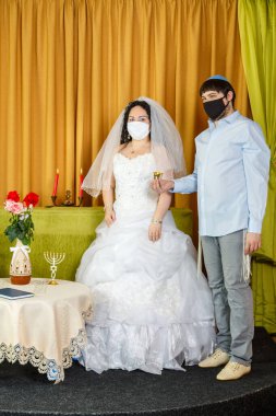Sinagogdaki chuppah töreni sırasında, gelin ve damat, yeni evlilerin elinde koruyucu maskeli bir bardak şarap tutarak damadın yanında dururlar. Dikey fotoğraf